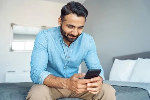 Indian man checking email message chatting social network using phone sit on bed Stock Photos