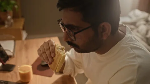 Indian Man Eating Sandwich While Working on Laptop at Home Stock Footage 337723048