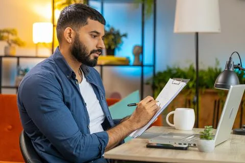 Indian man freelancer making notes on clipboard at home office using laptop Foto stock