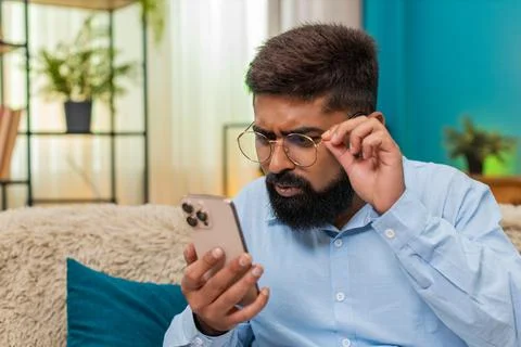 Indian man in glasses squints to read tiny smartphone text brings screen close Stock Photos