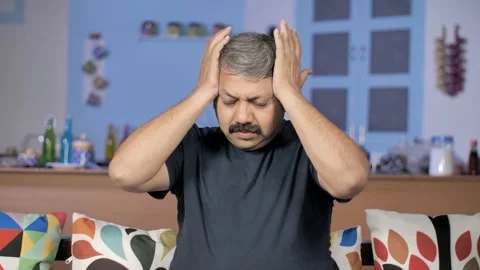 Indian man having a headache while sitting on a sofa - medical and healthcare 스톡 동영상 154022047