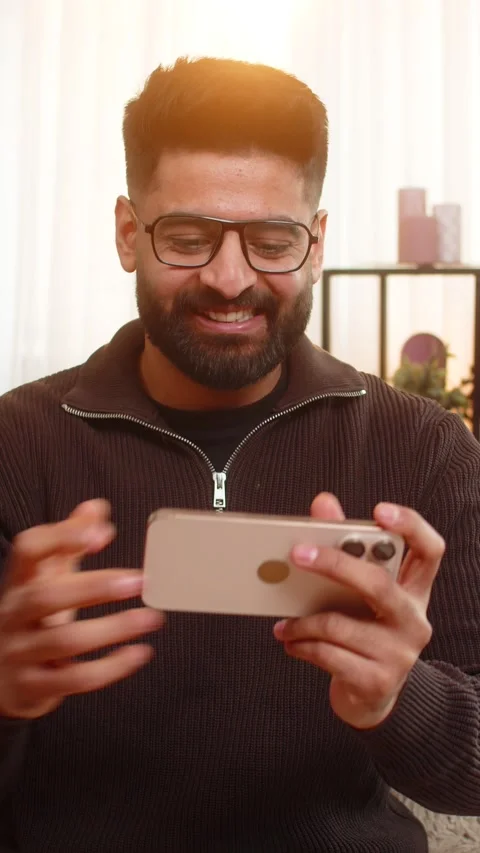 Indian man at home celebrating win with smartphone in hand clenched fist and Stock Footage 323353933