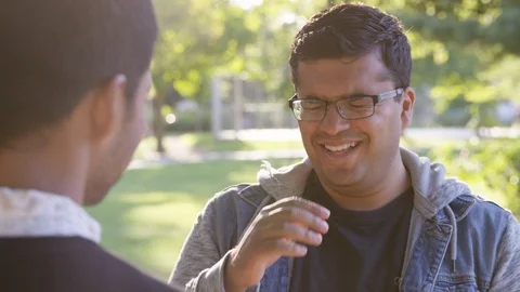 Indian man laughs at something his friend says while outside at the park - Slow Stock Footage 125098888