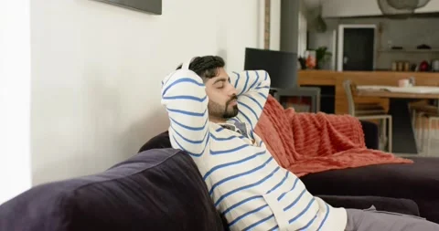 Indian man leaning back on sofa at home, placing hands behind head, relaxing Video stock 337537296