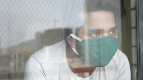 Indian man looking through a glass window is wearing a face mask 131084170