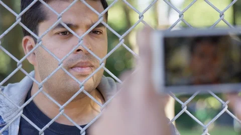 Indian man poses for the camera through a chainlink fence outside - Slow Motion Stock Footage 125091932