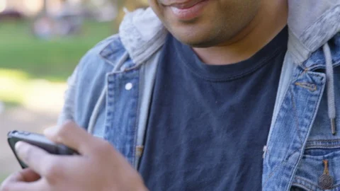 Indian man responds to something amusing on his friend's phone while at the park Stock Footage 125090299
