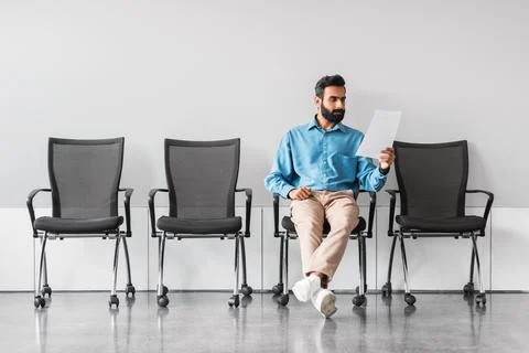 Indian man reviewing documents in sparse waiting room setting Stock Photos