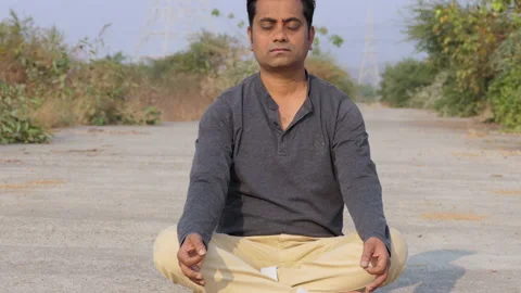 Indian man sitting with folded legs in the middle of the road and meditating Stock Footage 148456364