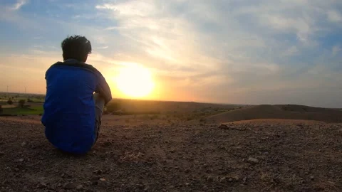 Indian man sitting in front of the sun during sunset on hill at Wankaner, Gujara Stockbeeldmateriaal 134403901