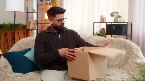 Indian man on sofa opens box and shakes head after discovering wrong item in 스톡 동영상 347033117