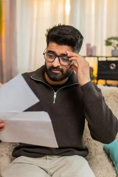Indian man on sofa opens envelope and looks sad after reading bad news in Foto stock