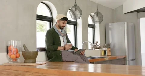 Indian man starting study scrolling tablet while sipping cup near bowl of Stock Footage 335454438