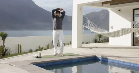 Indian man stepping onto mat on seaside terrace warming up stretching arms Stock Footage 338435155
