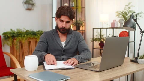 Indian man studies paper reports compares data with laptop focused look careful Stock Footage 347035587