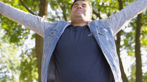 Indian man thrusts their arms out in triumph while holding their phone outside - Stock Footage 125095813
