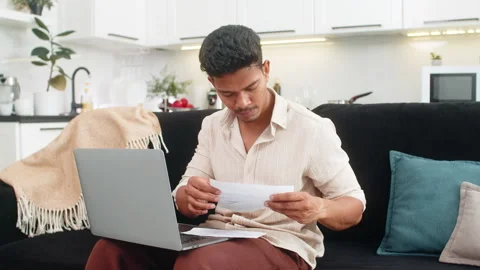 Indian man updates bill numbers in laptop spreadsheet checks docs and confirms Video stock 347044894