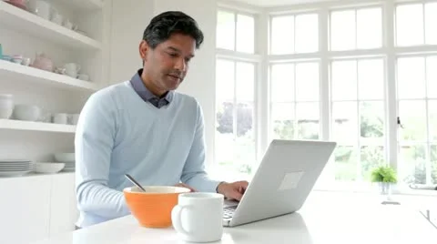 Indian Man Using Laptop Computer Whilst Eating Breakfast Stock Footage