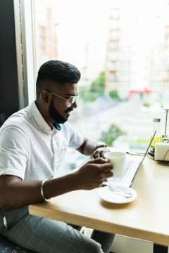 Indian man using laptop computer while drinking a cup hot milk tea, outdoor c Foto stock