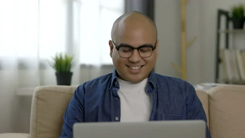 Indian man using laptop on sofa in living room texting on laptop sending message Stock Footage 153012060