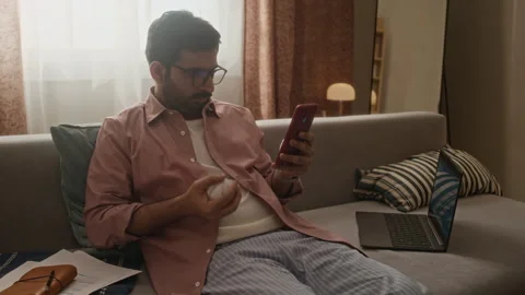 Indian Man Using Smartphone and Tossing Baseball While Working at Home Stock Footage 337723349