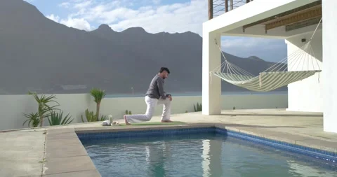 Indian man walking to mat by pool, lowering into lunge, stretching, standing, Stock Footage 335514394