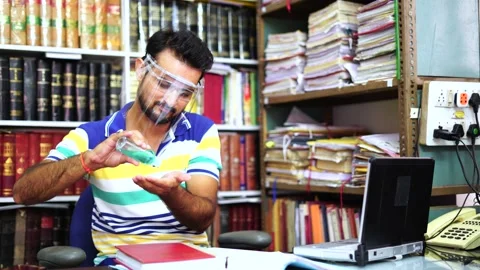 Indian man wearing face shield sanitize hand while working on laptop in office Stock Footage 138250654