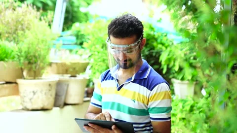 Indian Man wearing face shield using digital tablet at home outdoor garden Stock Footage 138258529