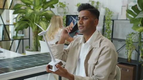 Indian Manager Talking on Smartphone and Holding Wind Turbine Model Stock Footage 276884683