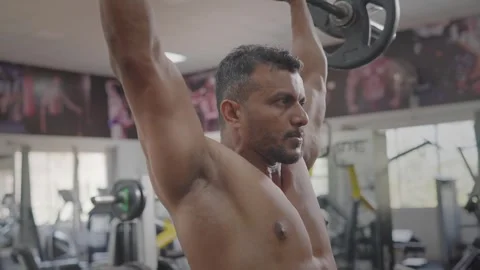 Indian middle aged fit man performs barbell shoulder press in a modern gym Stock Footage 341856500