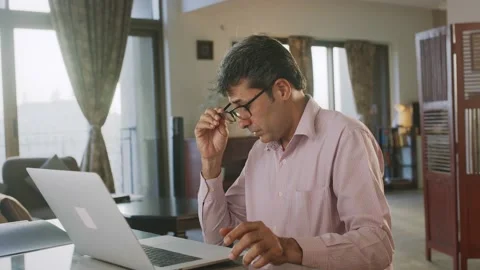 Indian Middle-aged Man busy over a Laptop looking tired takes off eye glasses Stock Footage 176784553