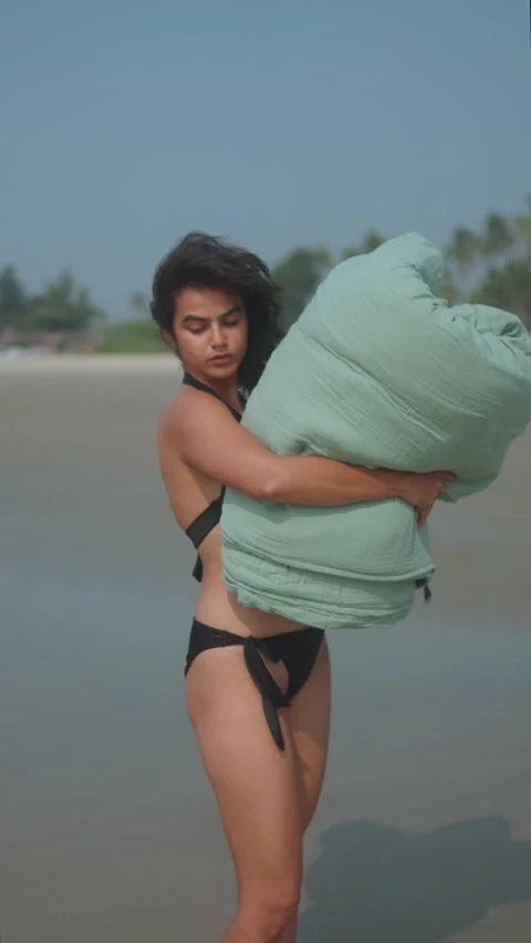 Indian model in black bikini standing on a tropical beach, holding a large 動画素材 320154495
