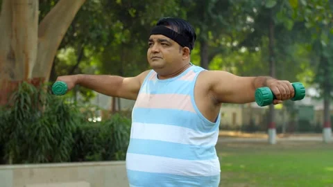 An Indian overweight man performing a workout in open gym - dumbbell lift, fi... Stock Footage 264016067