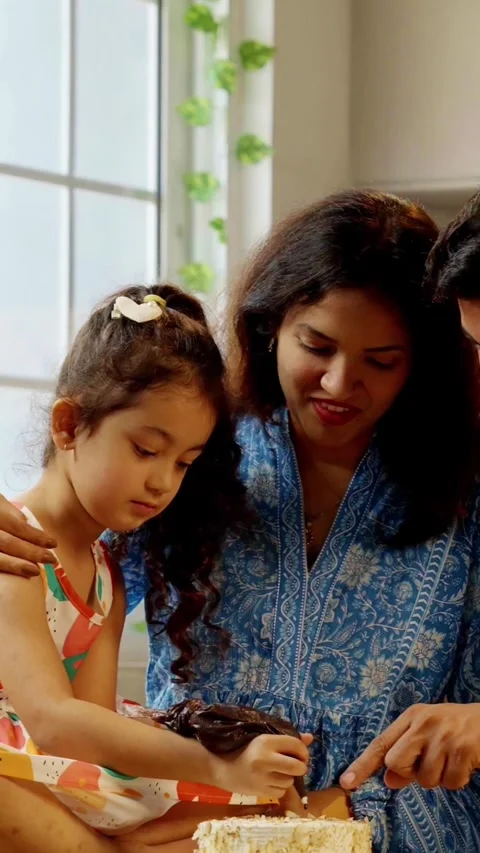 Indian smart young couple with small daughter decorating cake Video stock 343416277
