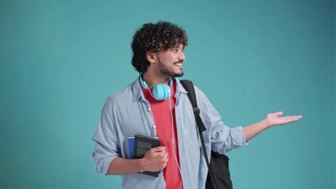 Indian student guy isolated on blue background with backpack on shoulders points Stock Footage 238768456