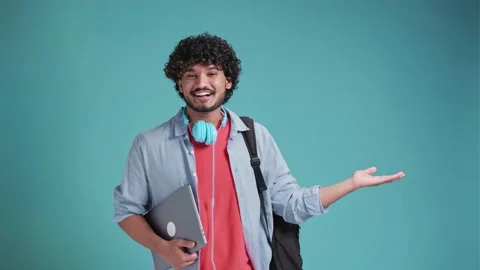 Indian student guy isolated on blue background with backpack on shoulders points Stock Footage 239096771