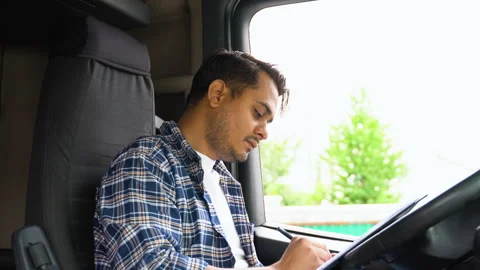 Indian truck driver checking shipment list while sitting in a truck cab Stock Footage 251834528