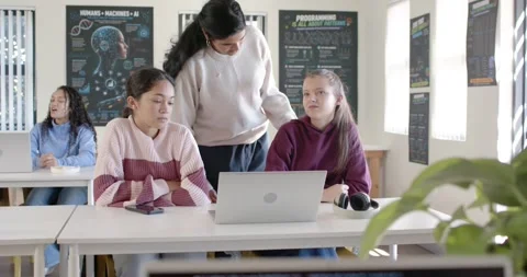 Indian tutor leaning, pointing to silver laptop helping youth females fixing Stock Footage 341029152
