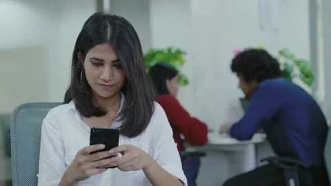Indian woman sitting on table while using smart phone for chatting. Видео 169385030
