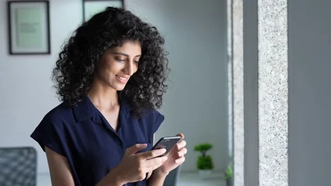 Indian woman standing on window while using smart phone for chatting with friend Stock Footage 170229416