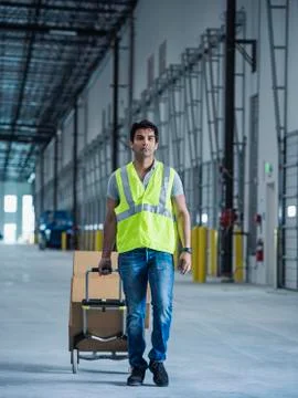 Indian worker pulling box on hand truck in warehouse Foto stock