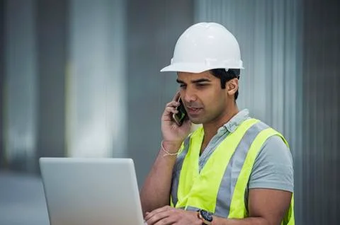Indian worker using laptop and cell phone in warehouse Stock Photos