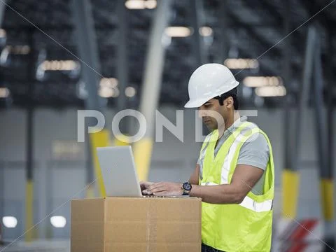 Indian Worker Using Laptop On Cardboard Box In Warehouse