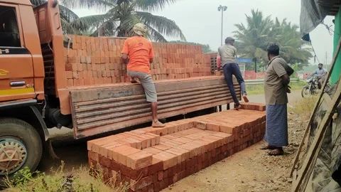 Indian workers unloading red bricks from the lorry trolley at construction si Stock Footage 223671995