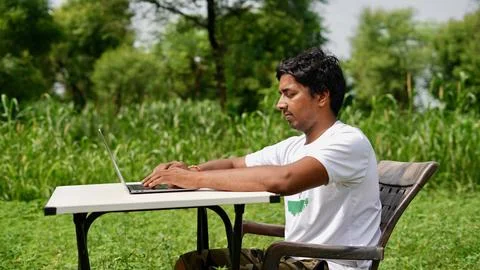 Indian young boy doing work from home. Man sitting on office table at garde.. Stock Photos