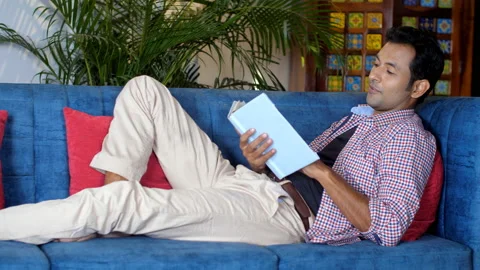An Indian young man reading a book while resting on the sofa in the living room Video stock 169918441