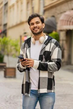 Indian young man using smartphone text messages browsing internet smiling at Stock Photos