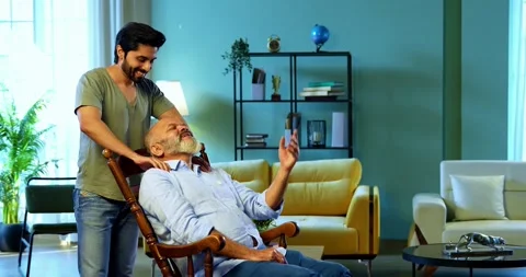 Indian young Son Massaging old Father Shoulders As He Relaxes On Rocking Chair Stock Footage 342778655
