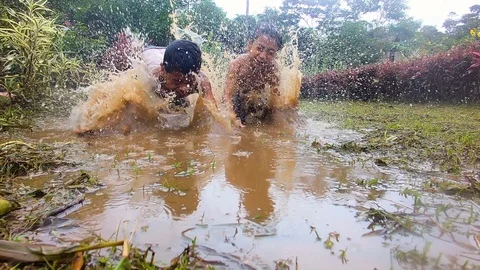 Indigenous kids throwing themself into a puddle in an amazon village slow motion Видео 113594029