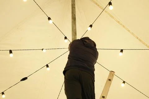 Individual adjusting decorative string lights on a tent ceiling, showcasing a Stock Photos